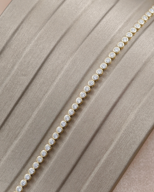 Close-up of round lab grown diamonds in individual yellow gold bezel settings along a tennis bracelet