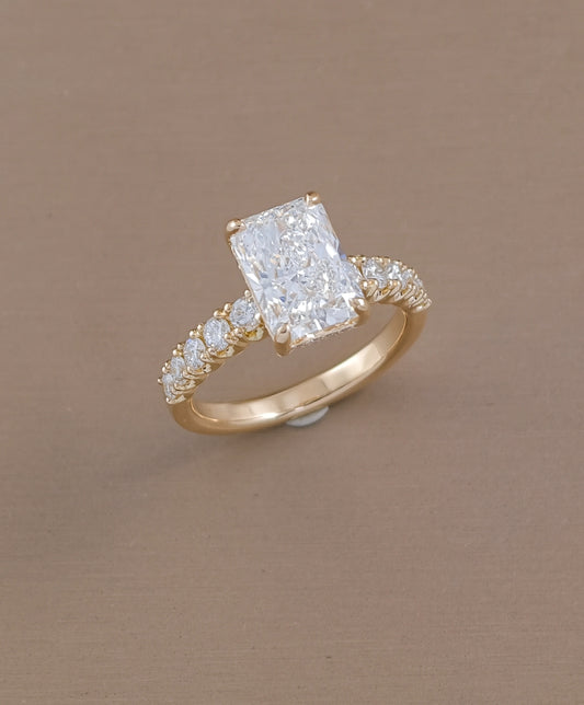 Angled view of radiant cut lab grown diamond ring with sparkling pavé diamonds on yellow gold band