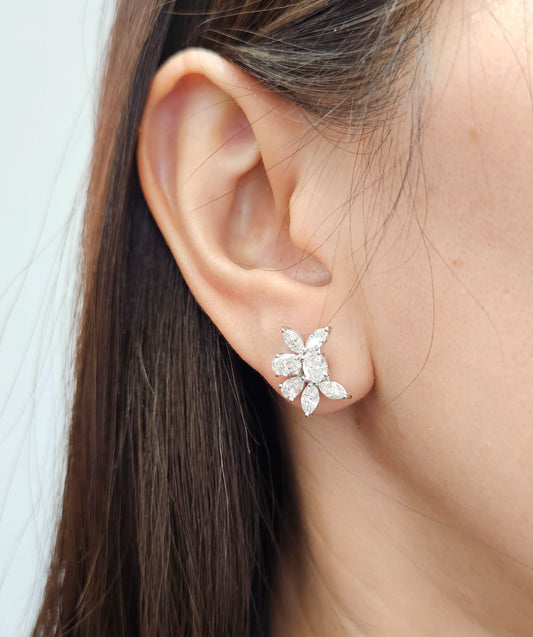 A close-up of a woman's ear wearing a small white gold flower stud earring with clear diamond 