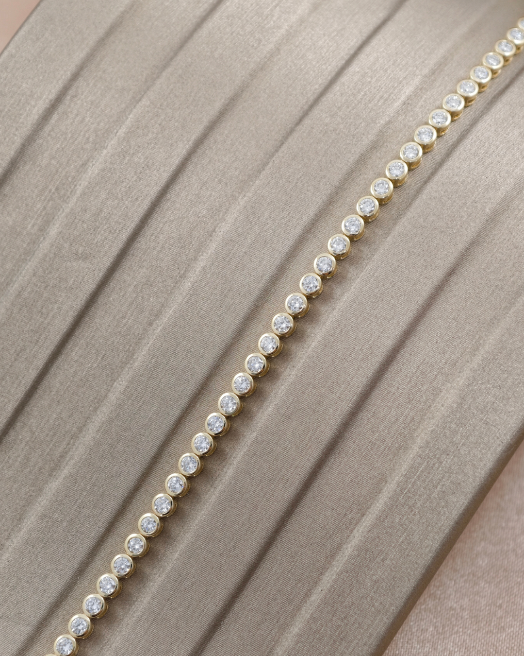 Close-up of round lab grown diamonds in individual yellow gold bezel settings along a tennis bracelet