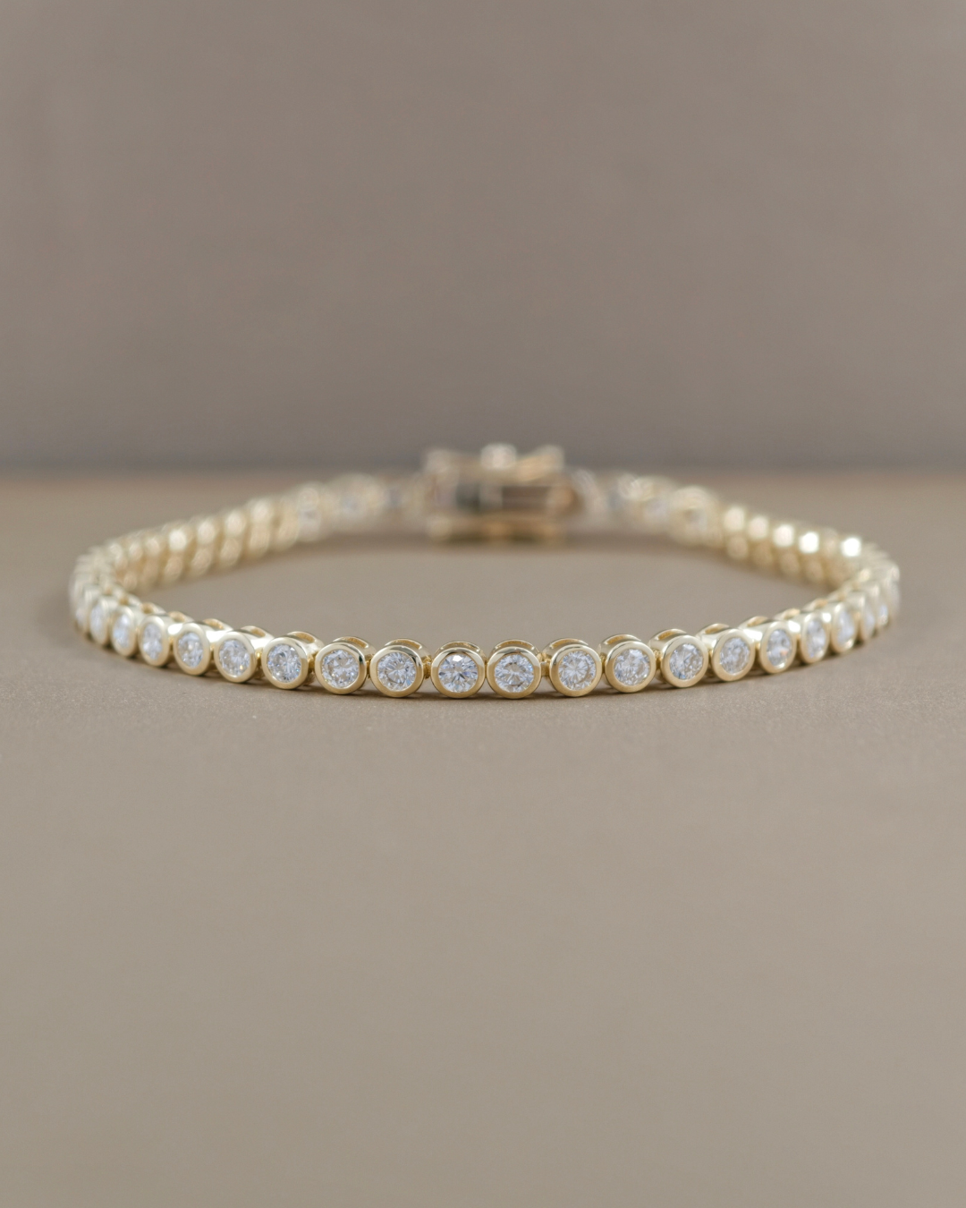 Yellow gold bezel set lab grown diamond tennis bracelet displayed horizontally, showing round diamonds and clasp
