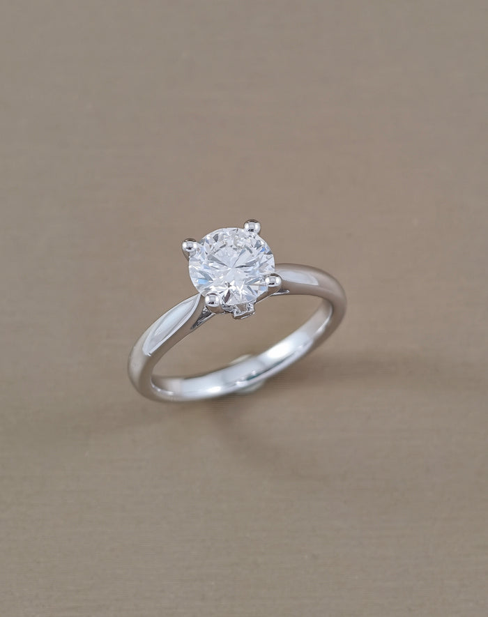 A classic solitaire engagement ring featuring a round brilliant-cut clear gemstone set in a polished white gold