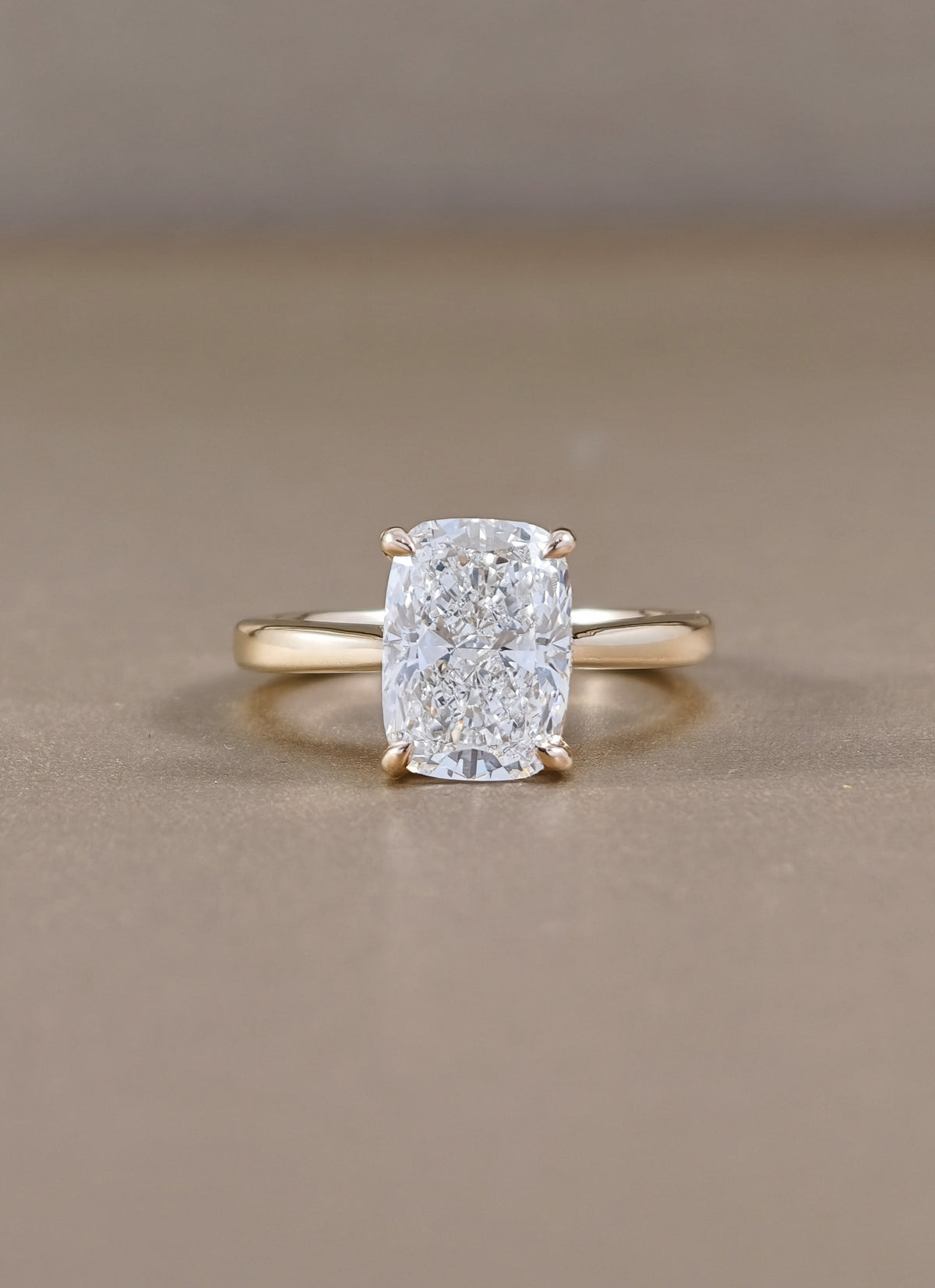 A yellow gold ring with a cushion-cut diamond lab grown set in a four-prong setting, 