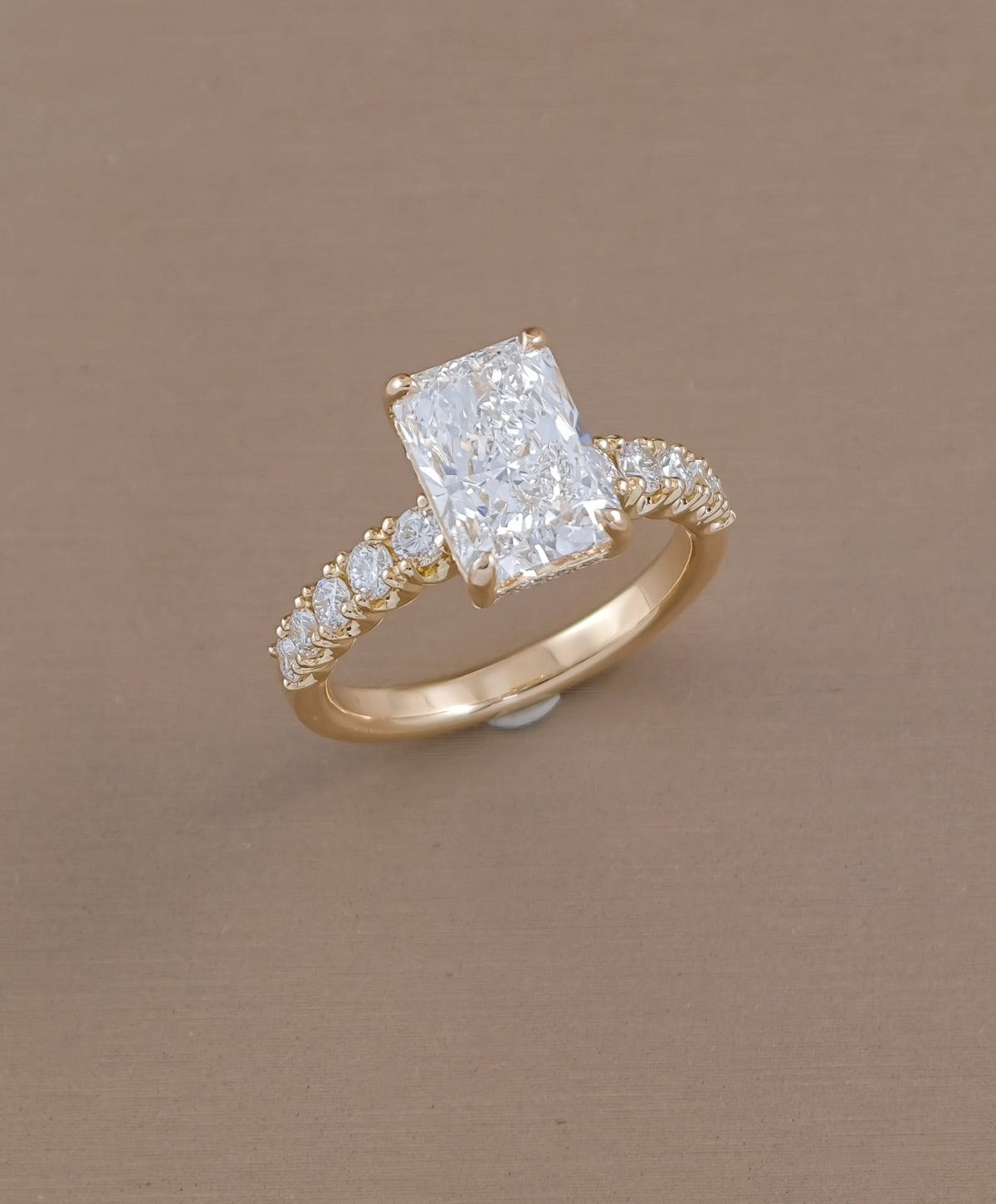 Angled view of radiant cut lab grown diamond ring with sparkling pavé diamonds on yellow gold band