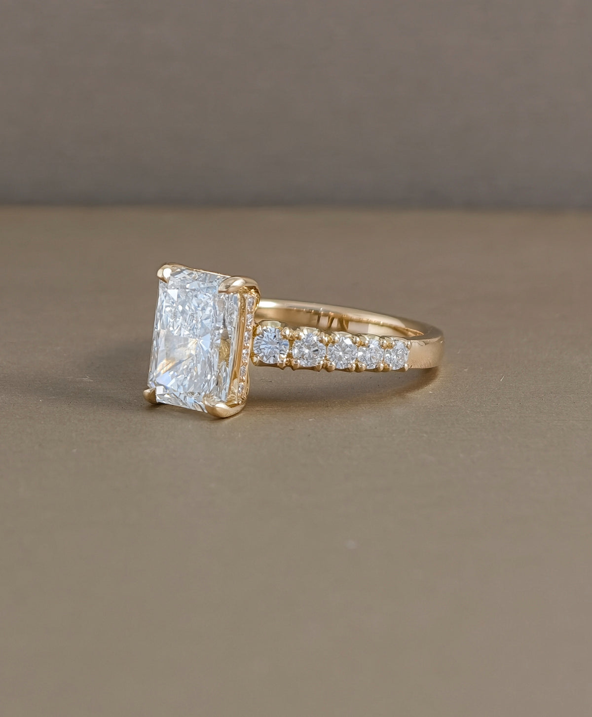 Side profile of radiant cut lab grown diamond engagement ring showing raised prong setting and pavé band