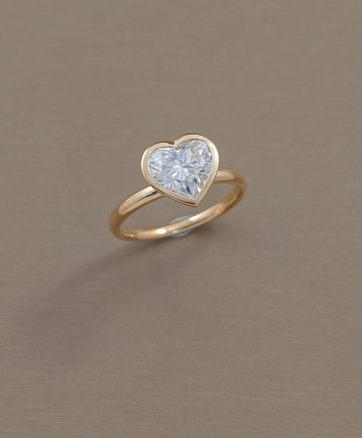 Angled view of heart cut lab grown diamond ring with polished yellow gold bezel setting