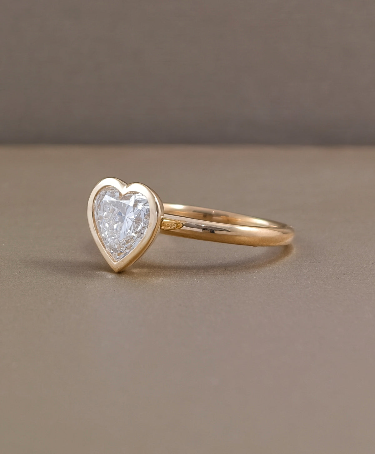 Side profile of heart shaped lab grown diamond engagement ring with smooth yellow gold bezel and polished band