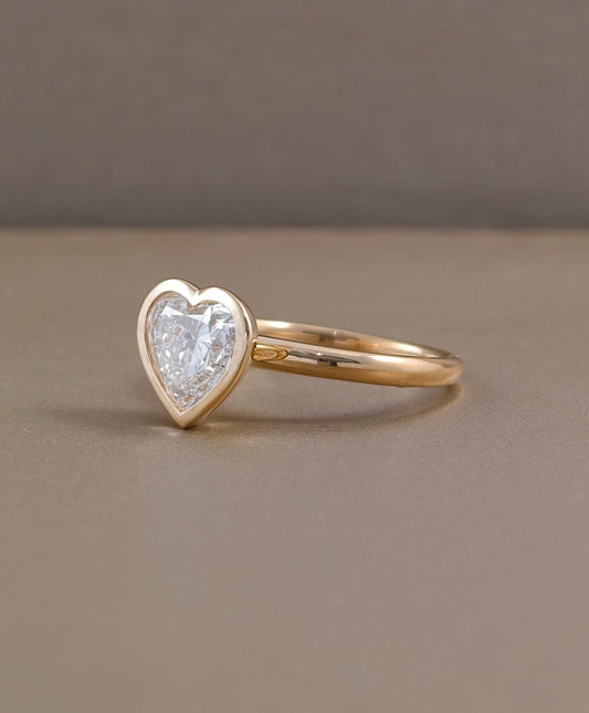 Side profile of heart shaped lab grown diamond engagement ring with smooth yellow gold bezel and polished band