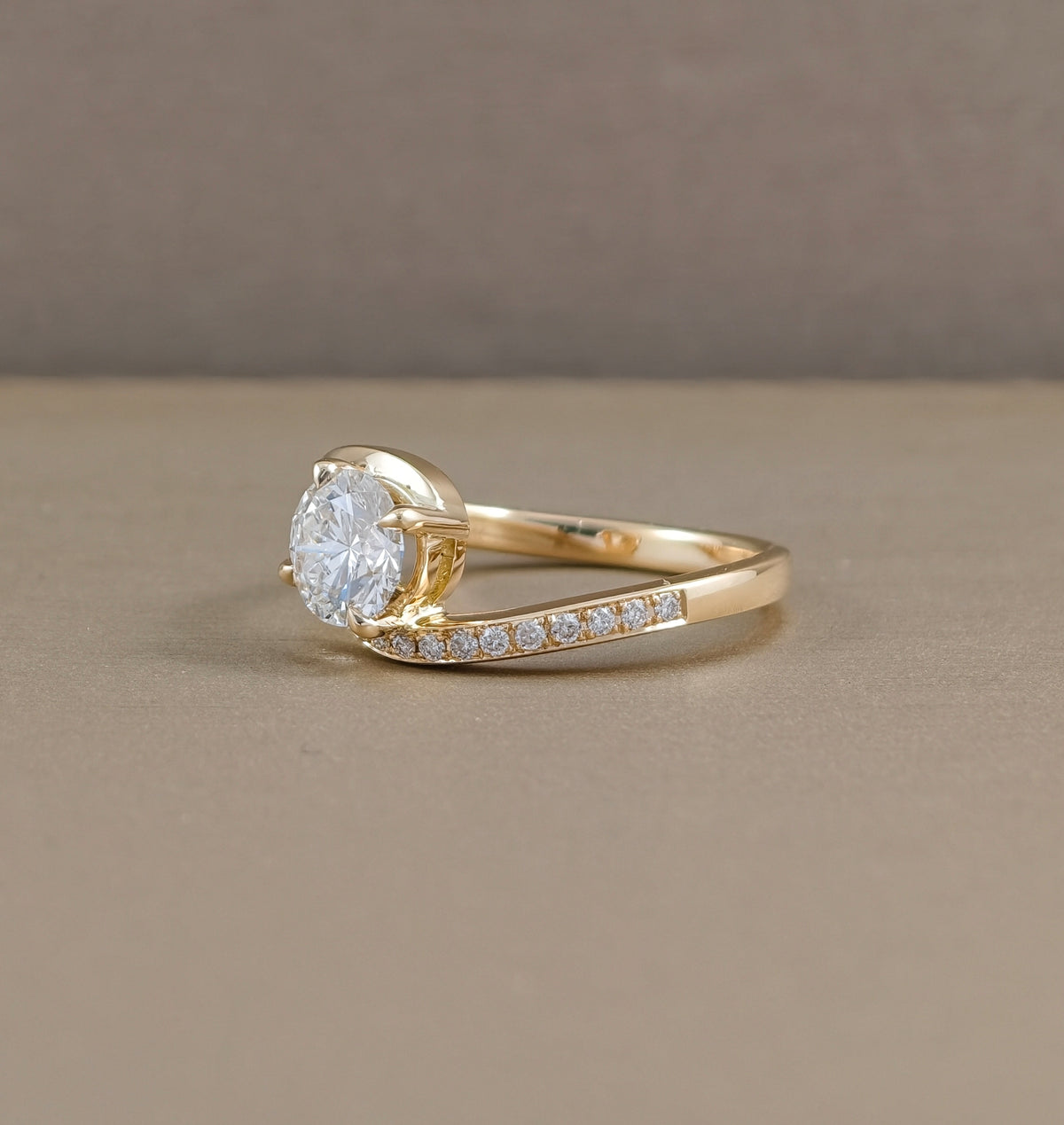 Round brilliant lab grown diamond twist engagement ring with pavé accents and yellow gold curved band