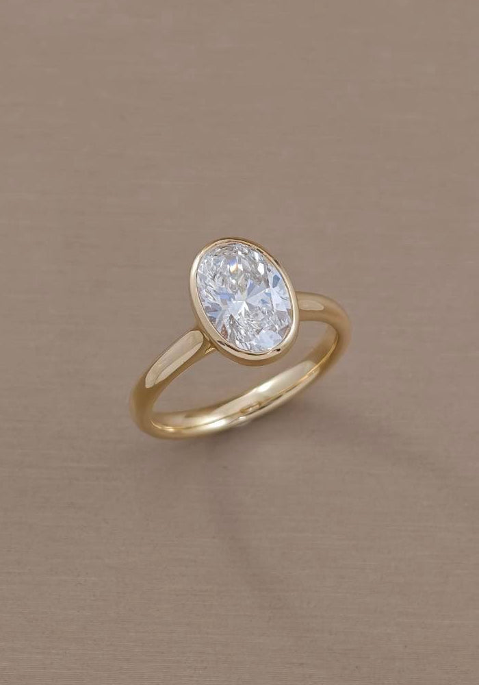 Profile view of oval bezel lab grown diamond engagement ring showing raised setting and yellow gold circular shank