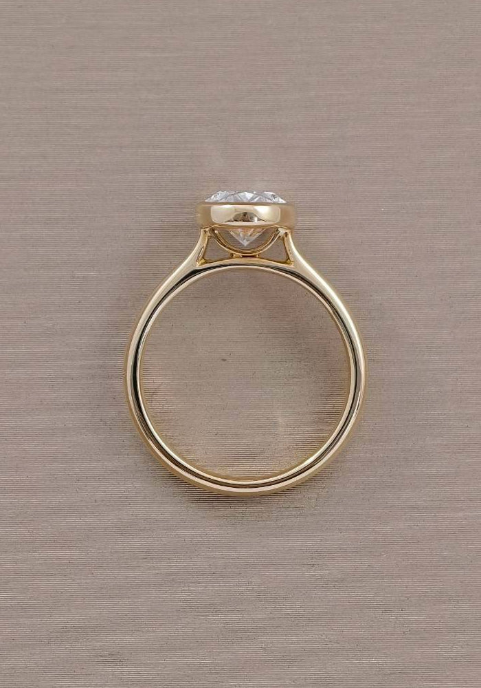 Profile view of oval bezel lab grown diamond engagement ring showing raised setting and yellow gold circular shank