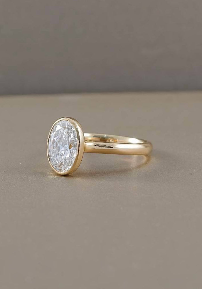 Side view of oval bezel lab grown diamond engagement ring with polished yellow gold band and raised diamond setting