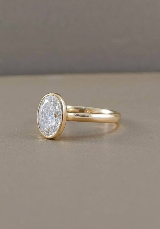 Side view of oval bezel lab grown diamond engagement ring with polished yellow gold band and raised diamond setting